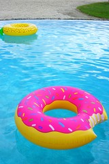 A pink plastic pool float shaped like a donut with sprinkles