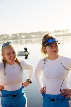 Female rowers with hands on hips at sunny lakeside