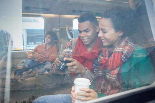 Young couple coffee looking at digital camera at window on passenger train