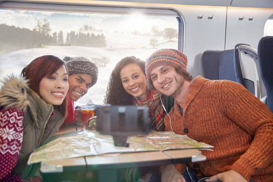 Happy young friends map taking selfie selfie stick on passenger train
