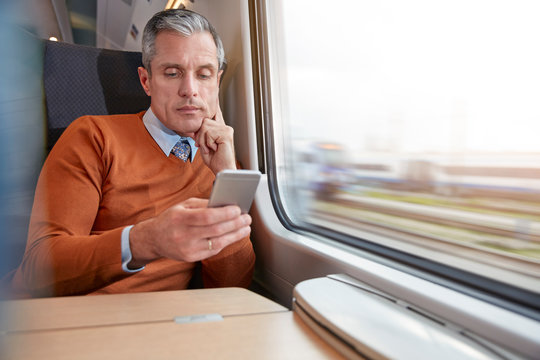 Focused businessman using smart phone at passenger train window
