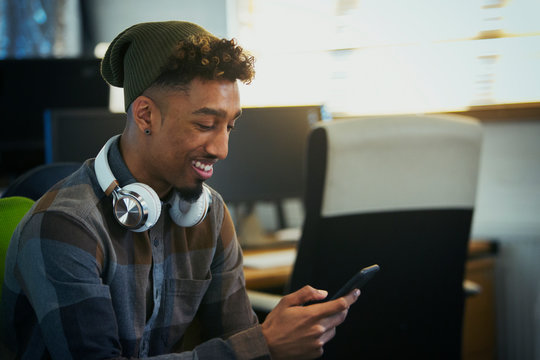 Smiling creative businessman headphones using smart phone in office