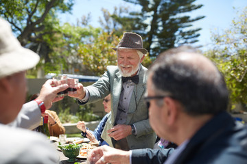 Senior man in suit bow tie toasting friends wine at sunny garden party