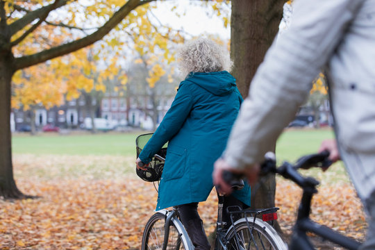 Senior woman bike riding among autumn leaves in park