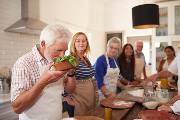 Active senior friends taking cooking class, smelling fresh basil