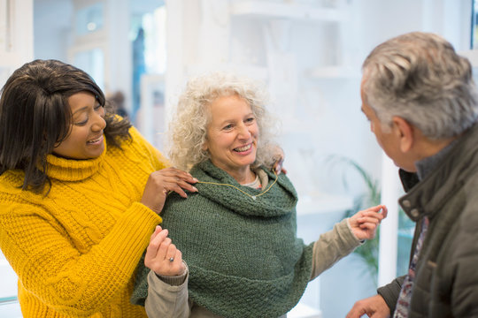 Sales assistant helping senior woman trying on jewelry in shop