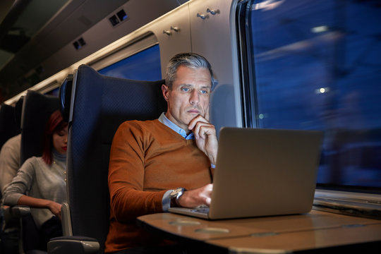 Focused businessman working at laptop on passenger train at night