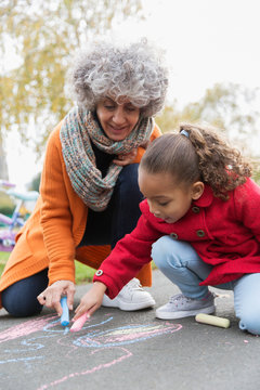 Grandmother And Granddaughter Drawing With Sidewalk Chalk