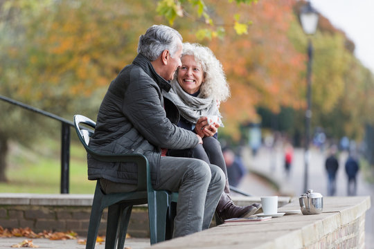 Smiling, affectionate active senior couple drinking tea in autumn park - Powered by Adobe