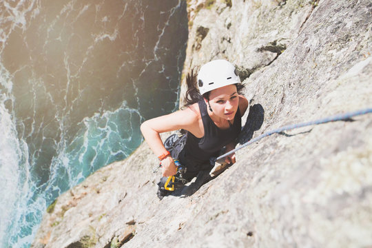 Focused, determined female rock climber scaling rock above sunny ocean