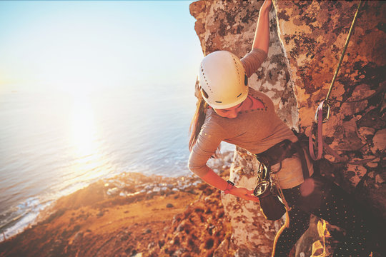 Female rock climber reaching for clip above sunny ocean