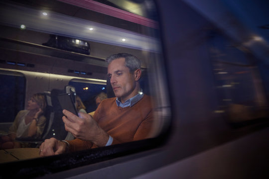 Businessman using smart phone at window on passenger train at night