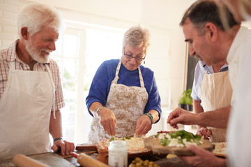Active senior friends making pizza in cooking class