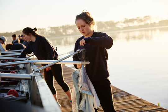 Female rowers preparing scull on sunny lakeside dock