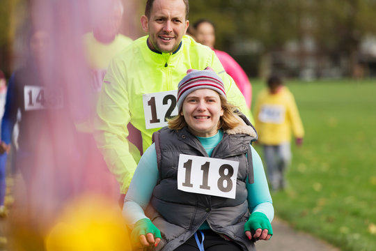 Portrait man pushing smiling woman in wheelchair at charity race in park