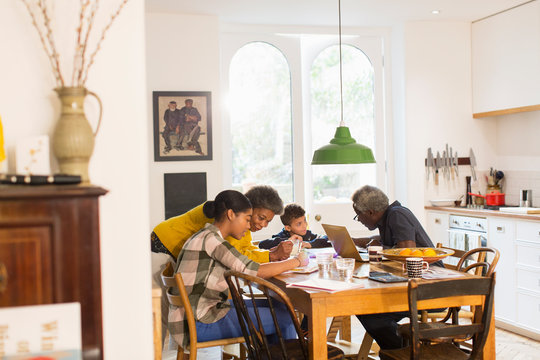 Grandparents helping grandchildren with homework at dining table