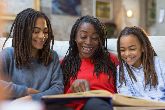 Mother and daughters looking at photo album on sofa