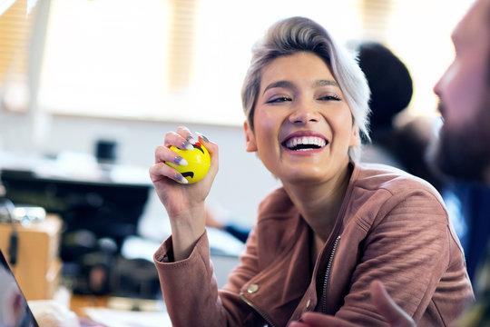 Laughing creative businesswoman squeezing stress ball in office