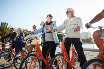 Active senior tourist friends bike riding on sunny boardwalk
