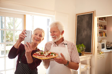 Smiling, confident senior couple taking selfie pizza at cooking class