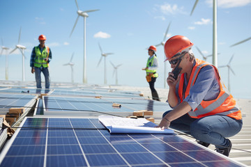 Engineer walkie-talkie blueprint at solar panel at sunny power plant