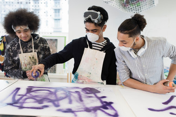 Teenage boys spray painting in high school art class