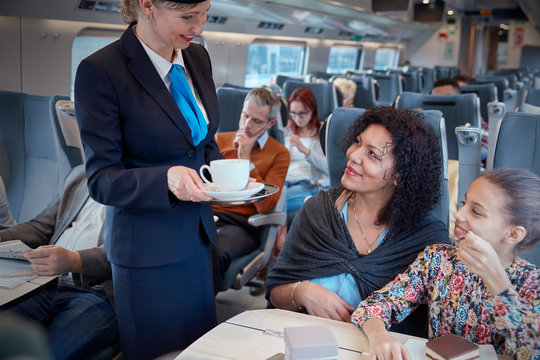 Attendant serving coffee to mother with daughter on passenger train