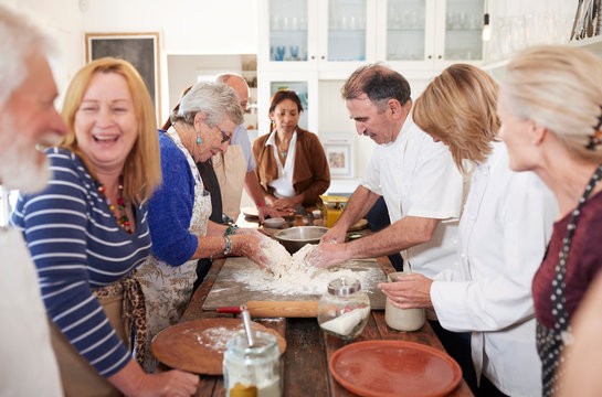 Senior friends enjoying pizza cooking class, making dough