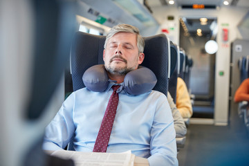 Tired businessman with neck pillow sleeping on passenger train
