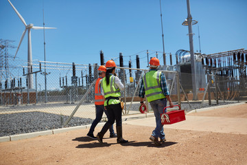 Engineers with toolbox walking at sunny wind turbine power plant