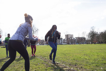 Woman cheering friend doing speed ladder drill in sunny park