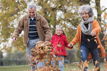 Playful grandparents and granddaughter kicking autumn leaves in park