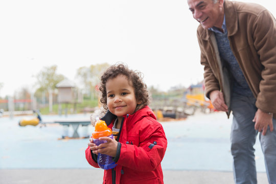 Grandfather watching toddler grandson with sippy cup at playground