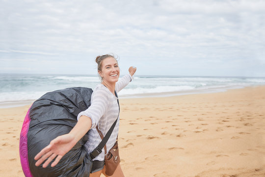 Portrait smiling, carefree young female paraglider parachute backpack on ocean beach