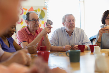Senior friends playing cards and drinking tea in community center