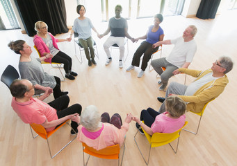 Active seniors holding hands in circle, meditating in community center
