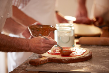 Close up man spreading marinara sauce on dough in pizza cooking class