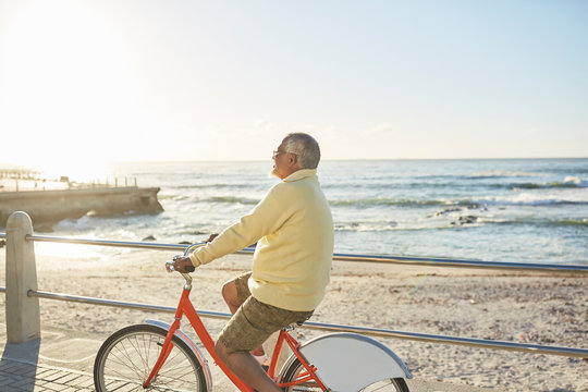 Active senior man tourist bike riding on sunny boardwalk along ocean