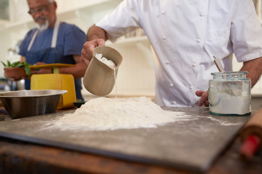 Close up chef pouring water into pizza dough flour nest in cooking class