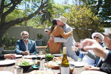 Friends toasting affectionate senior couple hugging at sunny garden party