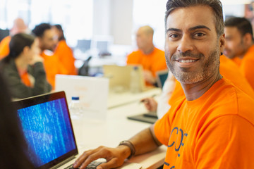 Portrait confident hacker at laptop coding for charity at hackathon