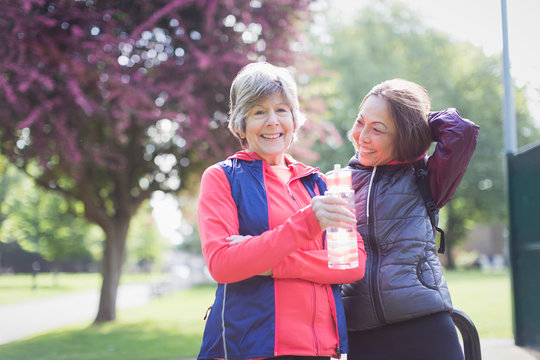 Portrait confident active senior female runner friends drinking water in park