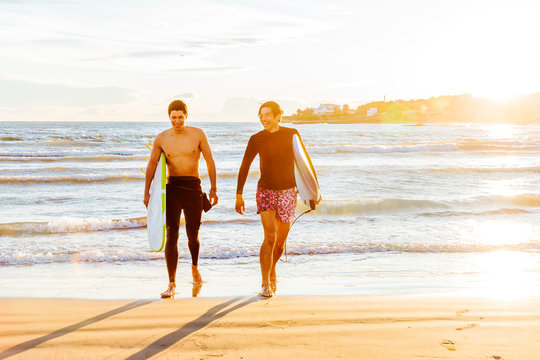 Male surfers carrying surfboards on sunny ocean beach