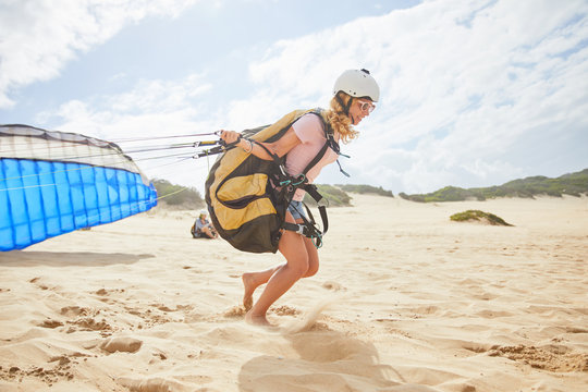 Female paraglider running with parachute on sunny beach