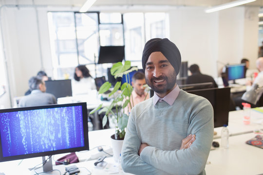 Portrait Smiling, Confident Indian Computer Programmer In Turban In Office