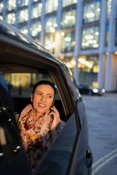 Smiling businesswoman talking on smart phone in crowdsourced taxi at night