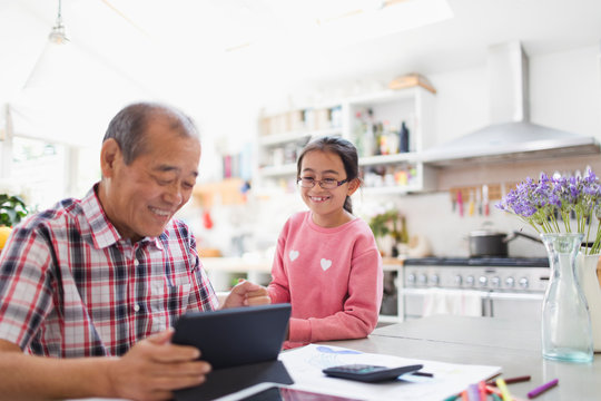 Grandfather and granddaughter using digital tablet in kitchen