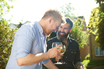 Happy male gay couple drinking wine in sunny garden