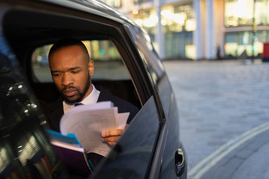 Businessman reading paperwork in crowdsourced taxi at night