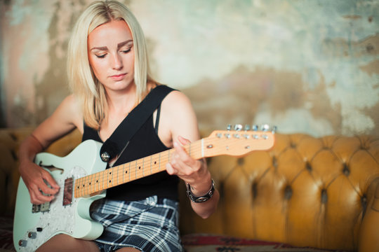Young woman playing electric guitar on sofa - Powered by Adobe